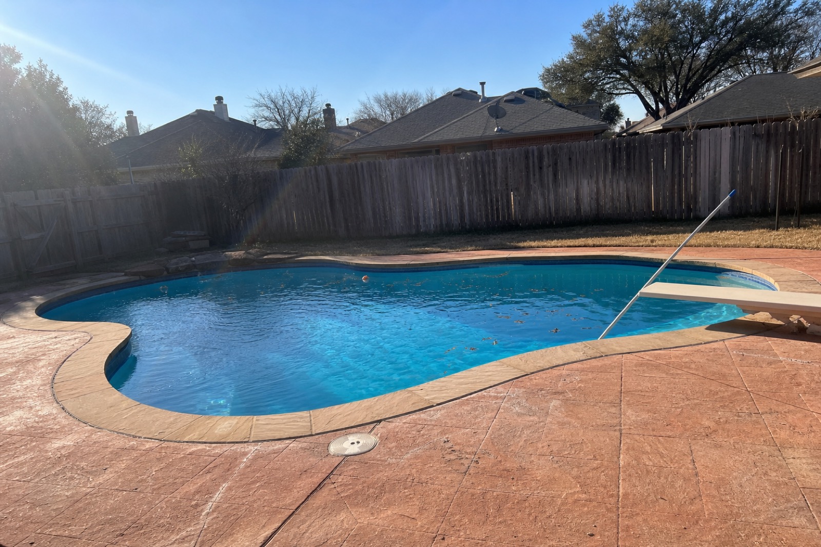 Kidney-shaped backyard pool with weathered cedar fence and terracotta deck